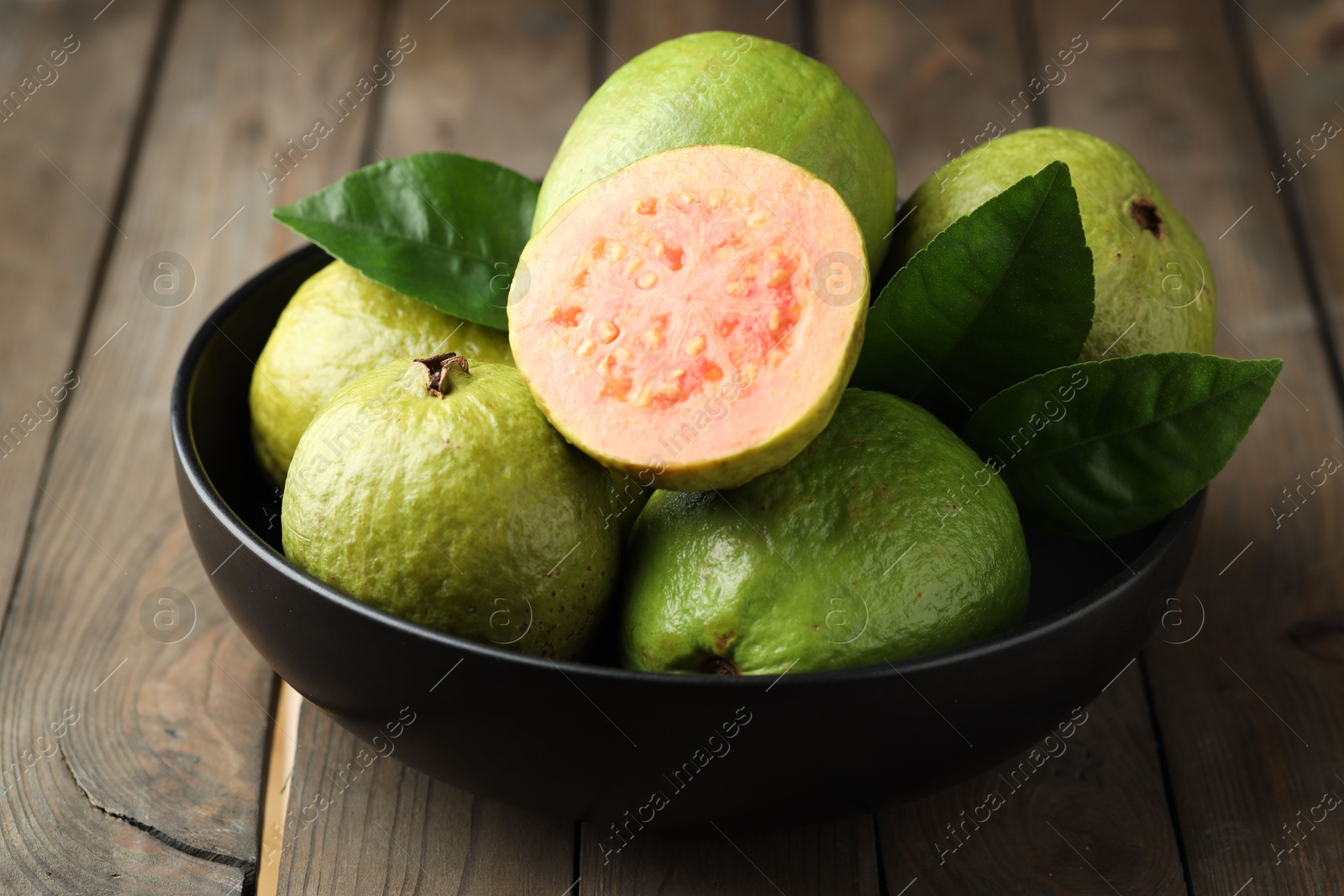 Photo of Fresh guava fruits in bowl on wooden table, closeup