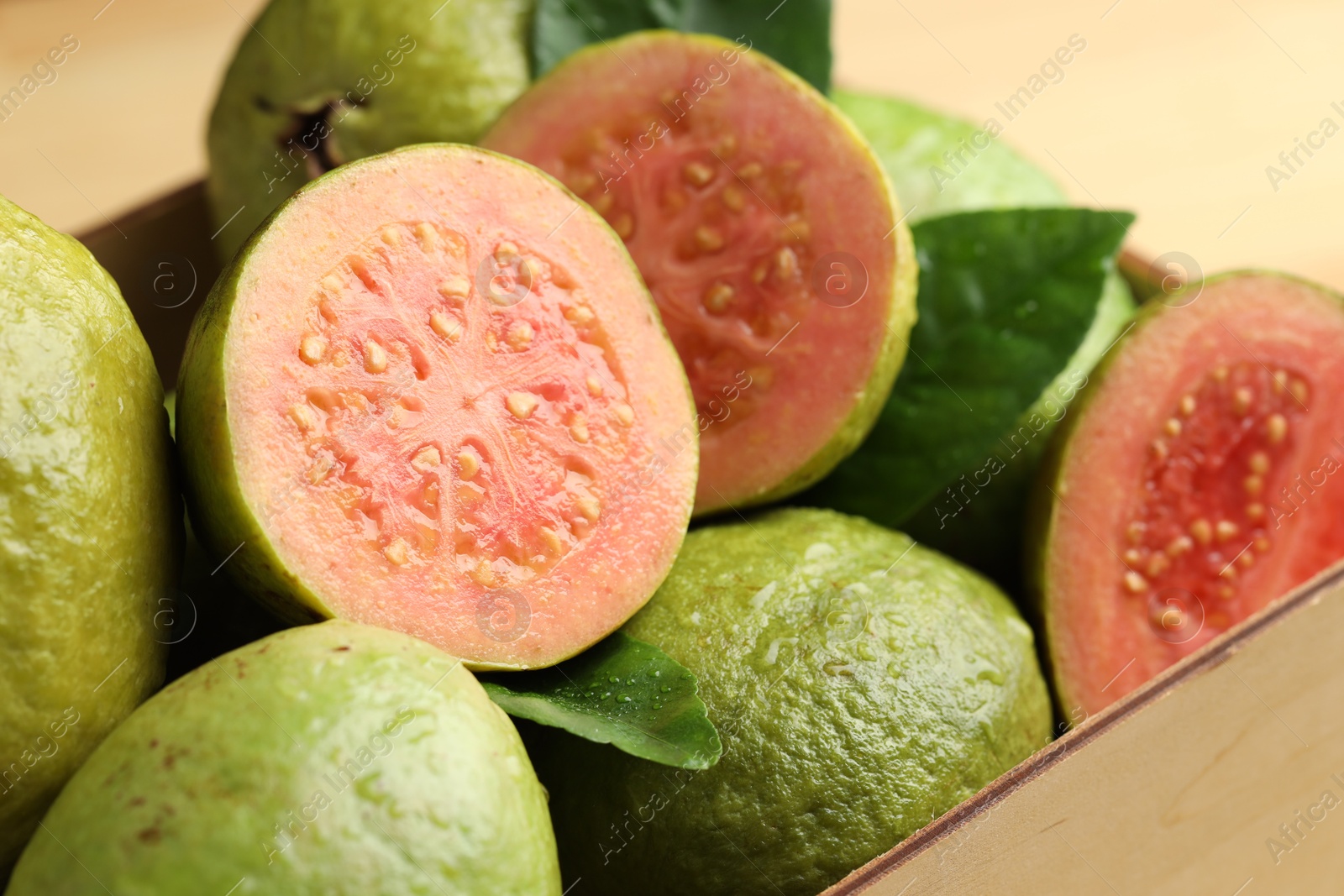 Photo of Fresh cut and whole guava fruits in wooden crate, closeup