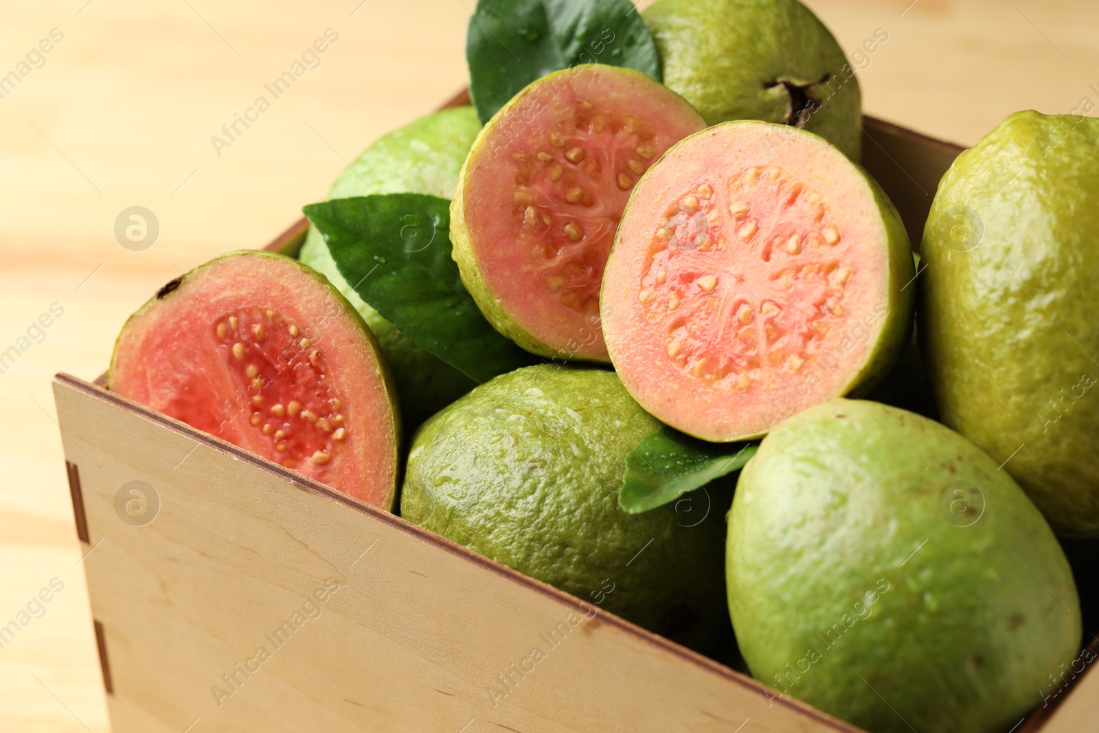 Photo of Fresh cut and whole guava fruits in wooden crate on table, closeup