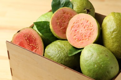 Photo of Fresh cut and whole guava fruits in wooden crate on table, closeup