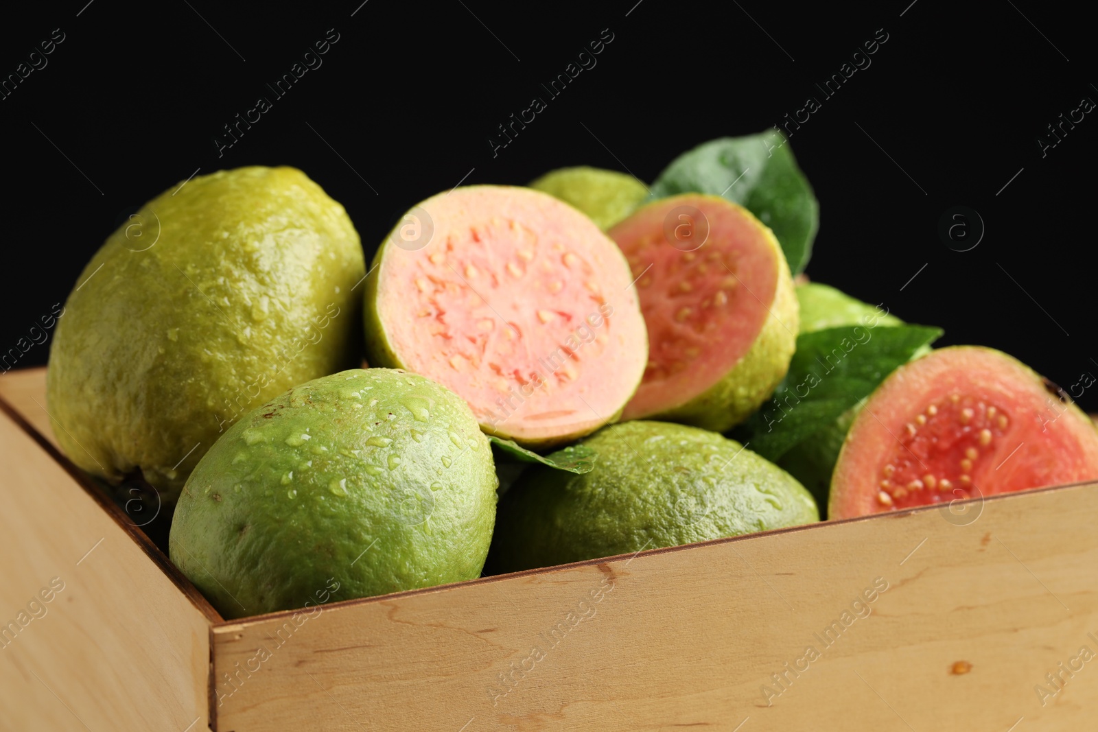 Photo of Fresh cut and whole guava fruits in wooden crate against black background, closeup