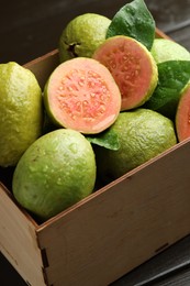 Photo of Fresh cut and whole guava fruits in wooden crate on black table, closeup