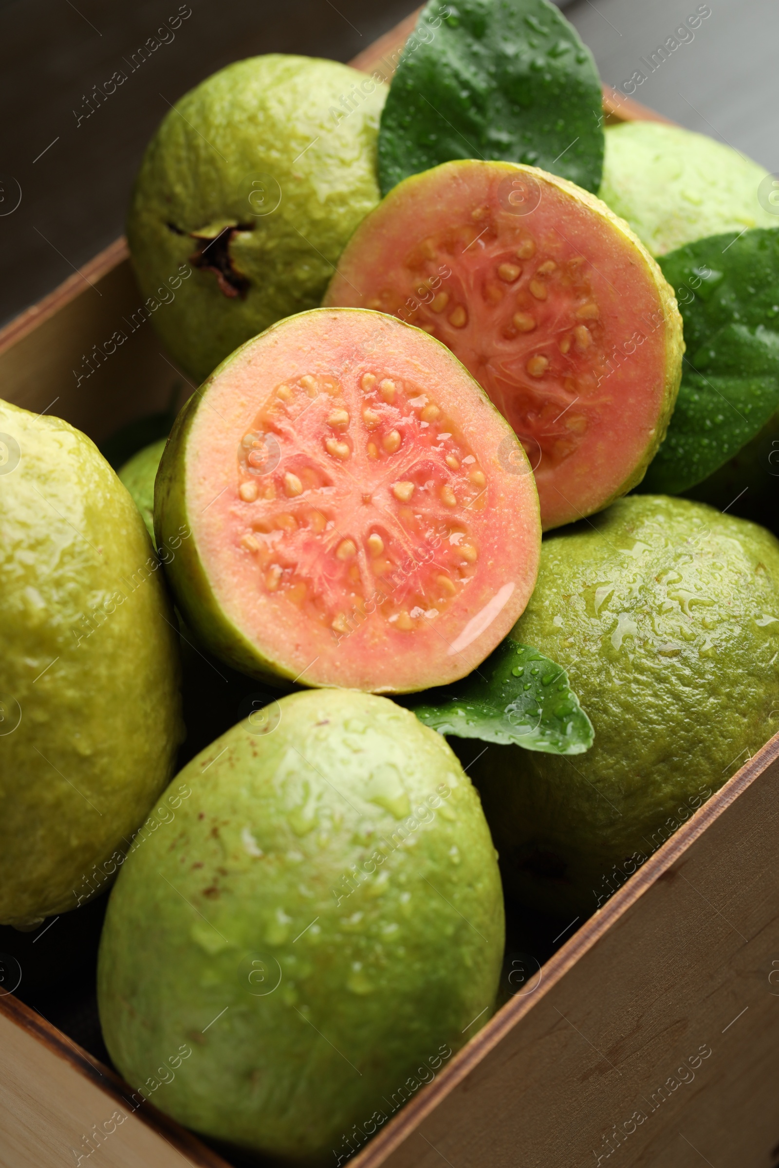 Photo of Fresh cut and whole guava fruits in wooden crate on table, closeup