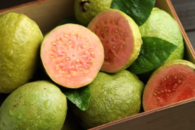 Photo of Fresh cut and whole guava fruits in wooden crate on table, closeup