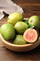 Photo of Fresh cut and whole guava fruits in bowl on wooden table, closeup