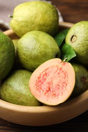 Photo of Fresh cut and whole guava fruits in bowl on table, closeup