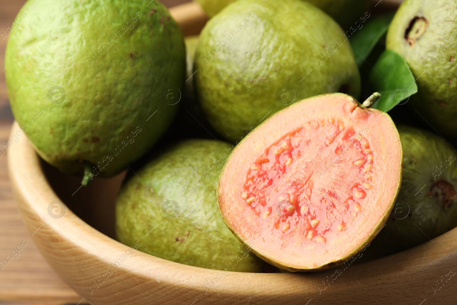 Photo of Fresh cut and whole guava fruits in bowl on table, closeup