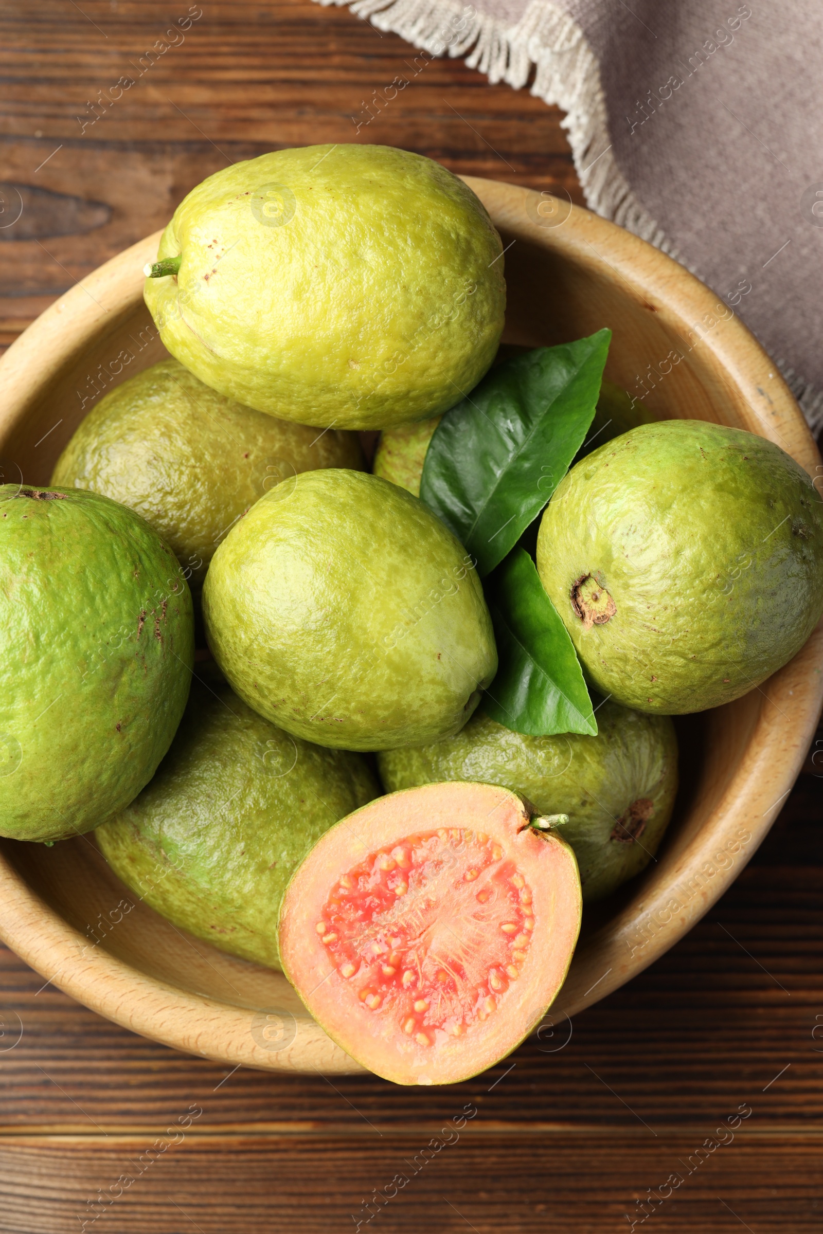 Photo of Fresh cut and whole guava fruits in bowl on wooden table, top view