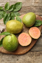 Photo of Fresh whole and cut guava fruits on wooden table, flat lay