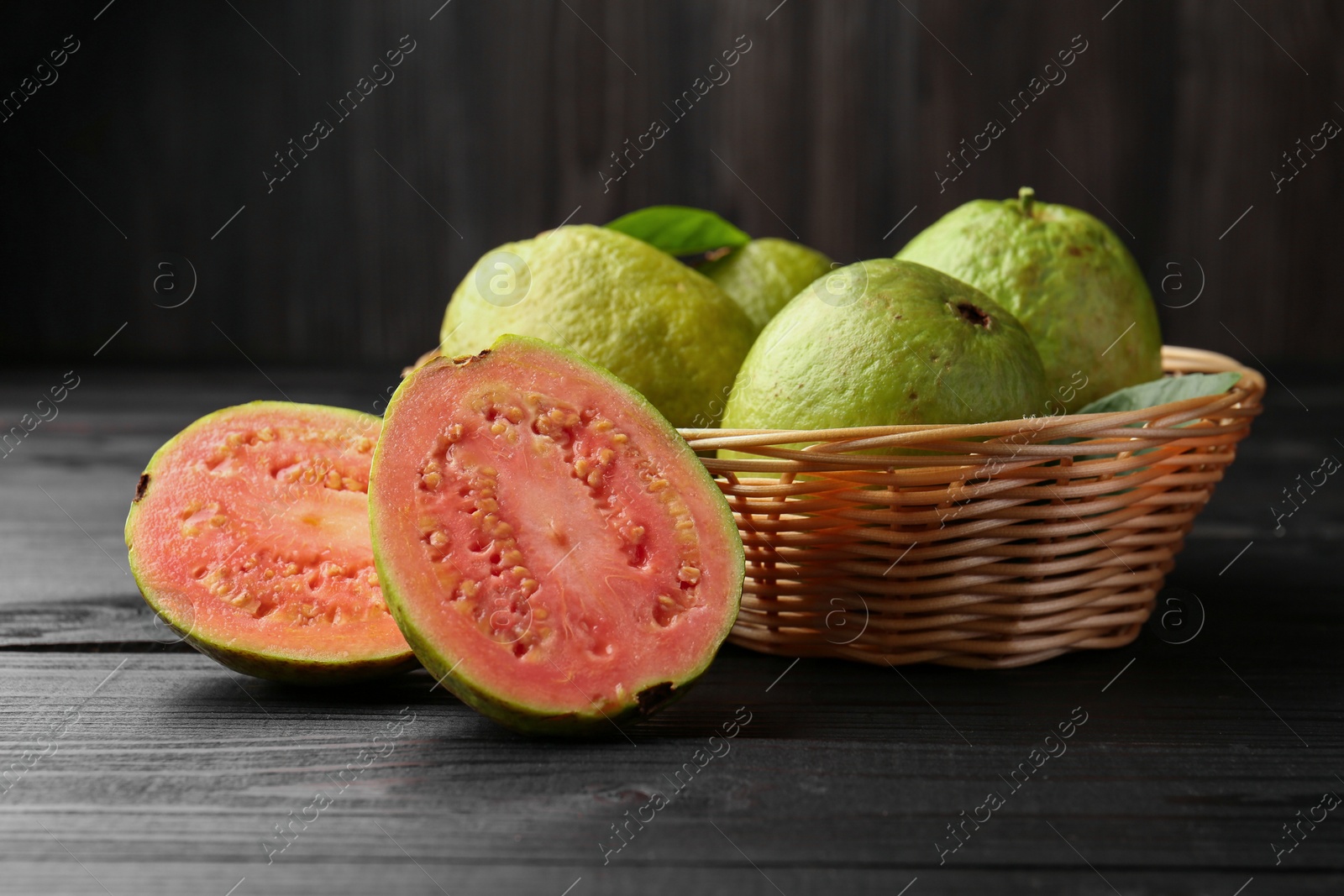 Photo of Fresh whole and cut guava fruits on black wooden table, closeup