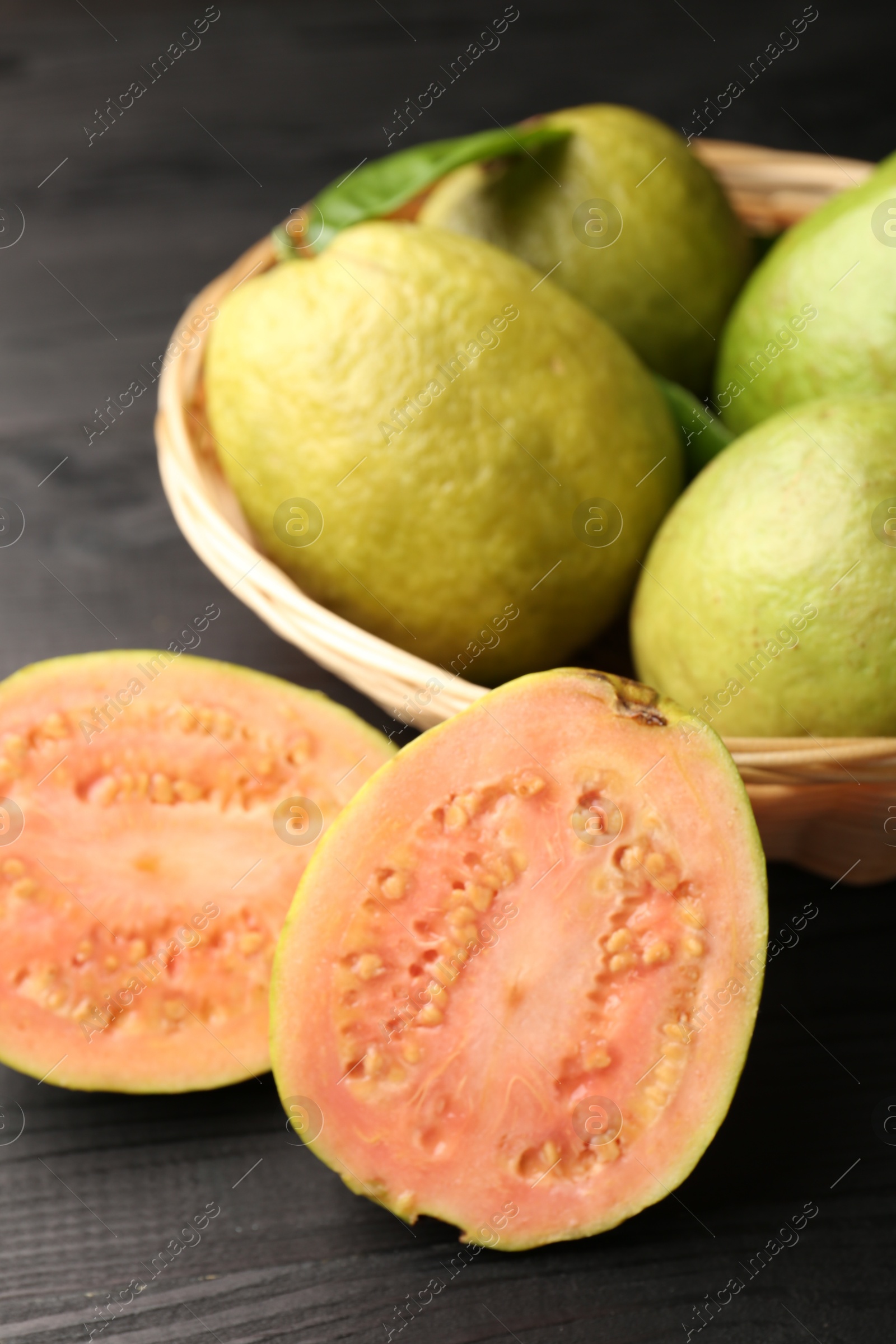 Photo of Fresh whole and cut guava fruits on black wooden table, closeup