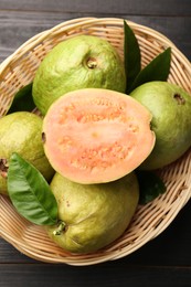 Photo of Fresh whole and cut guava fruits in wicker basket on black wooden table, top view