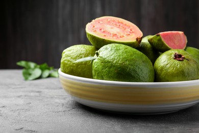 Photo of Fresh whole and cut guava fruits in bowl on grey textured table, closeup