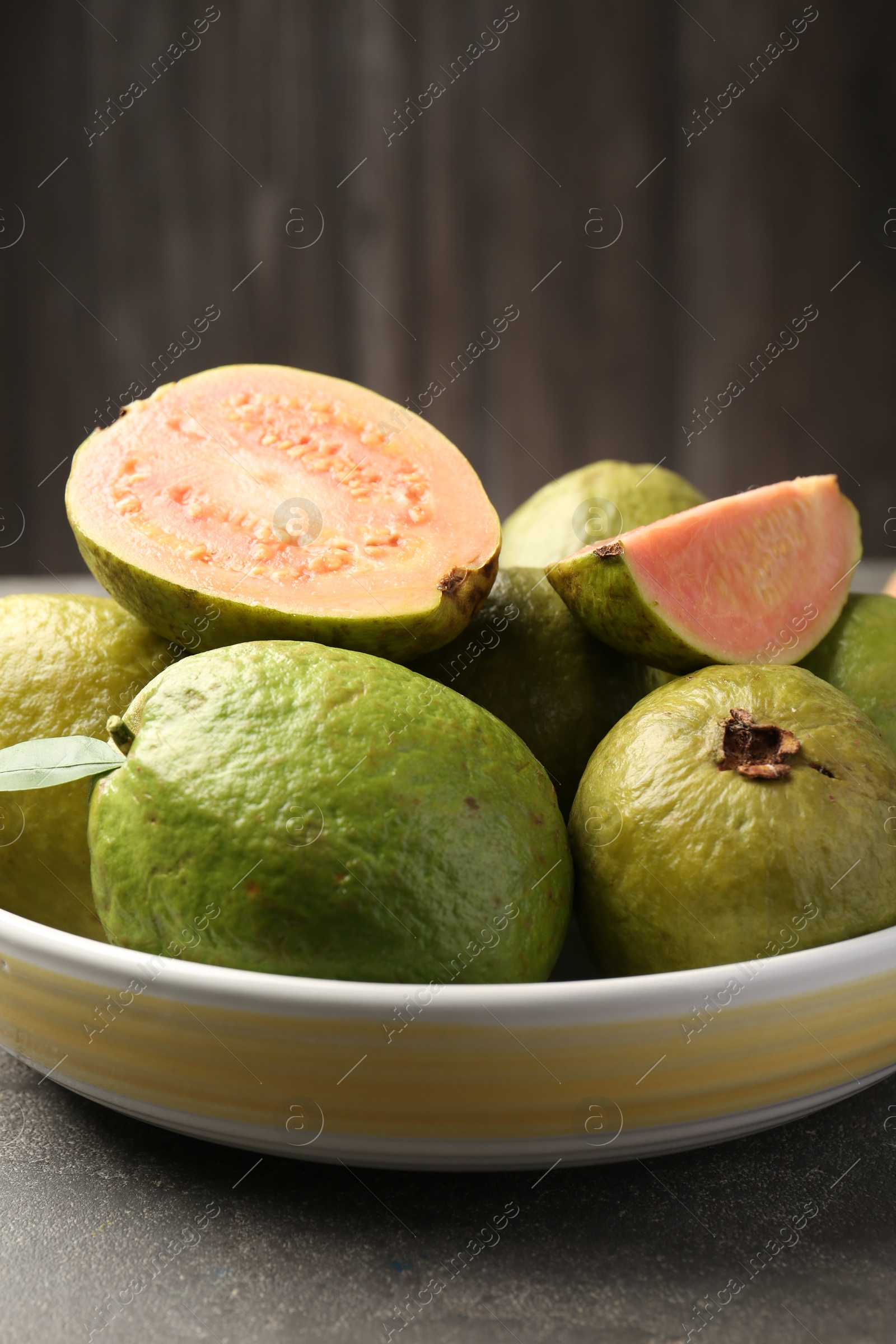 Photo of Fresh whole and cut guava fruits in bowl on grey textured table, closeup