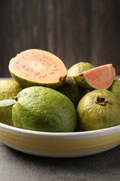 Photo of Fresh whole and cut guava fruits in bowl on grey textured table, closeup