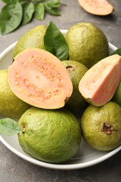 Photo of Fresh whole and cut guava fruits in bowl on grey textured table, closeup