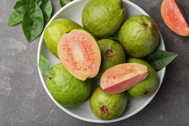 Photo of Fresh whole and cut guava fruits in bowl on grey textured table, top view