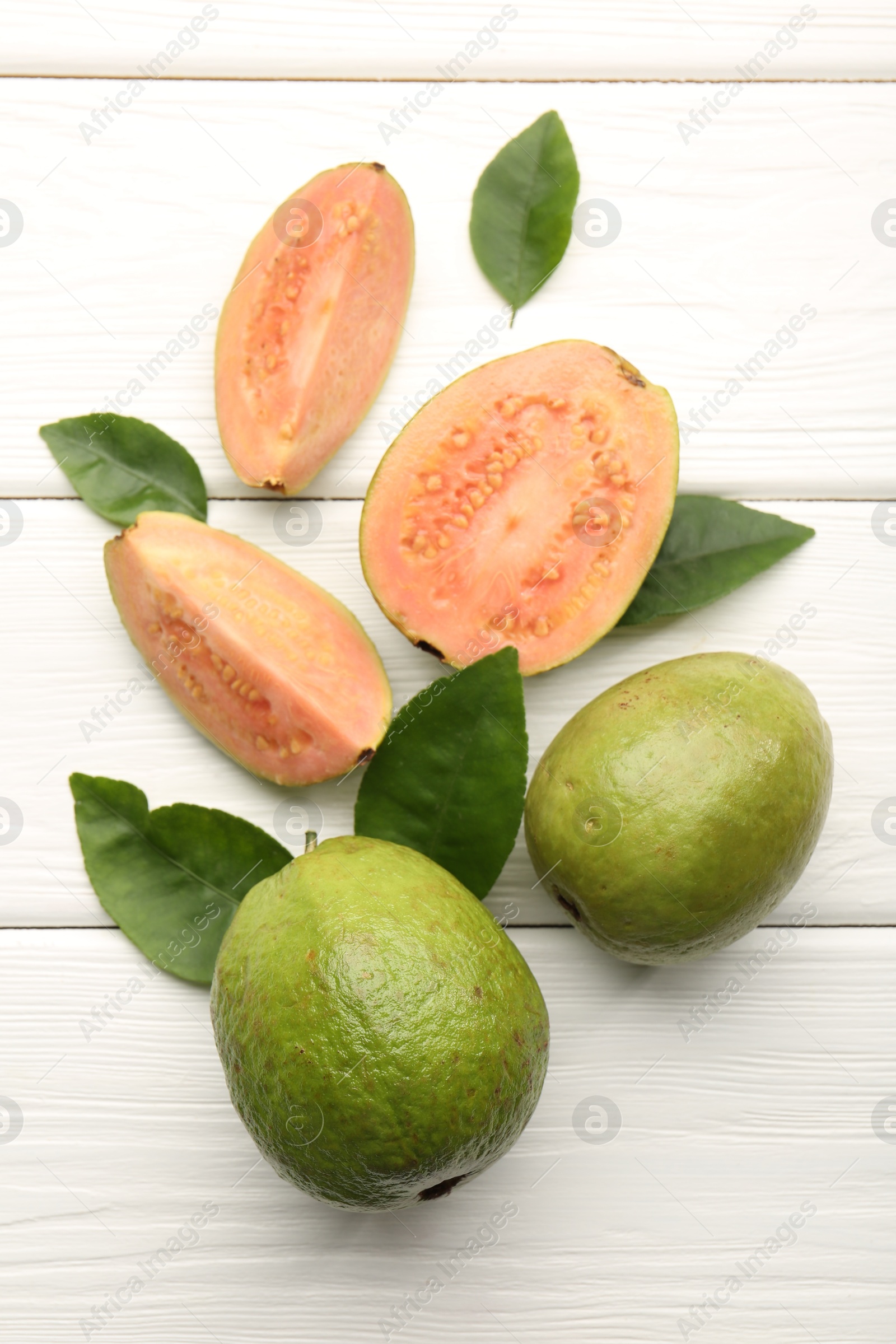 Photo of Fresh whole and cut guava fruits on white wooden table, flat lay