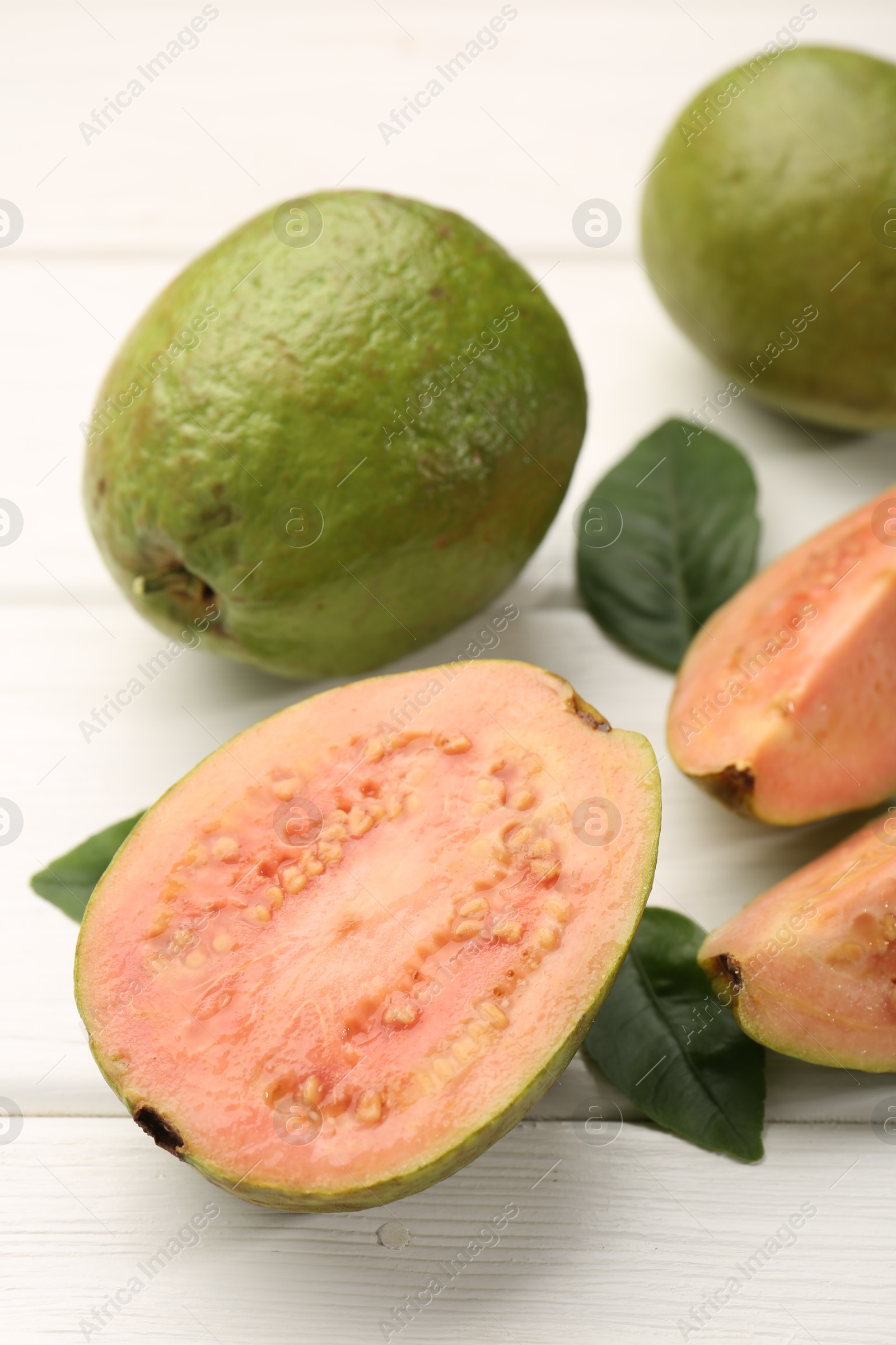 Photo of Fresh whole and cut guava fruits on white wooden table, closeup