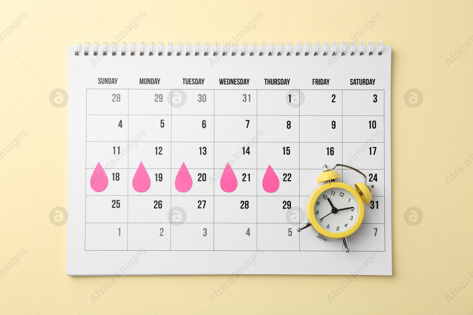 Photo of Menstruation. Calendar with marked dates and alarm clock on beige background, top view