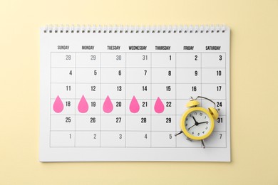 Photo of Menstruation. Calendar with marked dates and alarm clock on beige background, top view