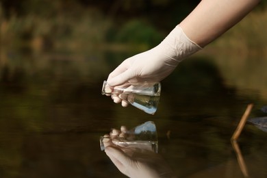 Photo of Examination of water quality. Researcher taking water sample from lake outdoors, closeup