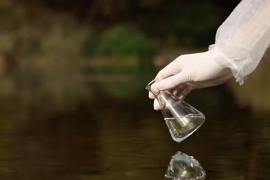 Photo of Examination of water quality. Researcher holding flask with sample from lake outdoors, closeup. Space for text