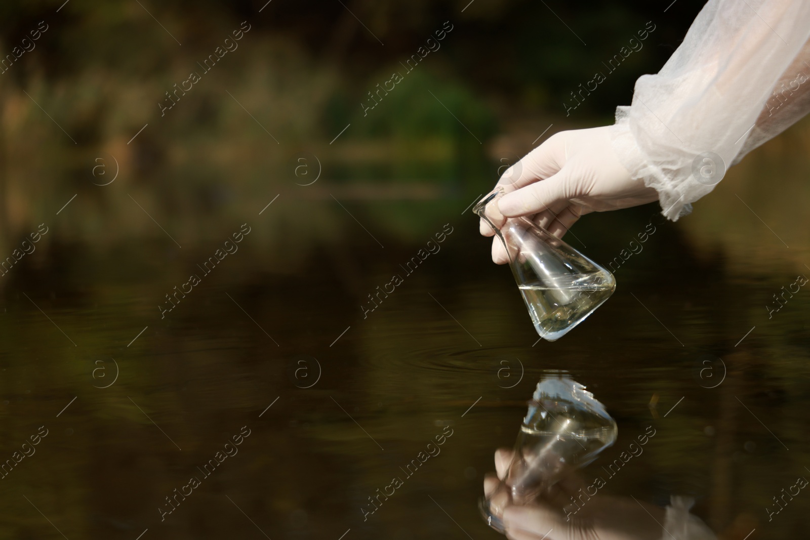 Photo of Examination of water quality. Researcher holding flask with sample from lake outdoors, closeup. Space for text