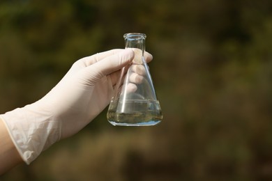 Photo of Examination of water quality. Researcher holding flask with sample outdoors, closeup