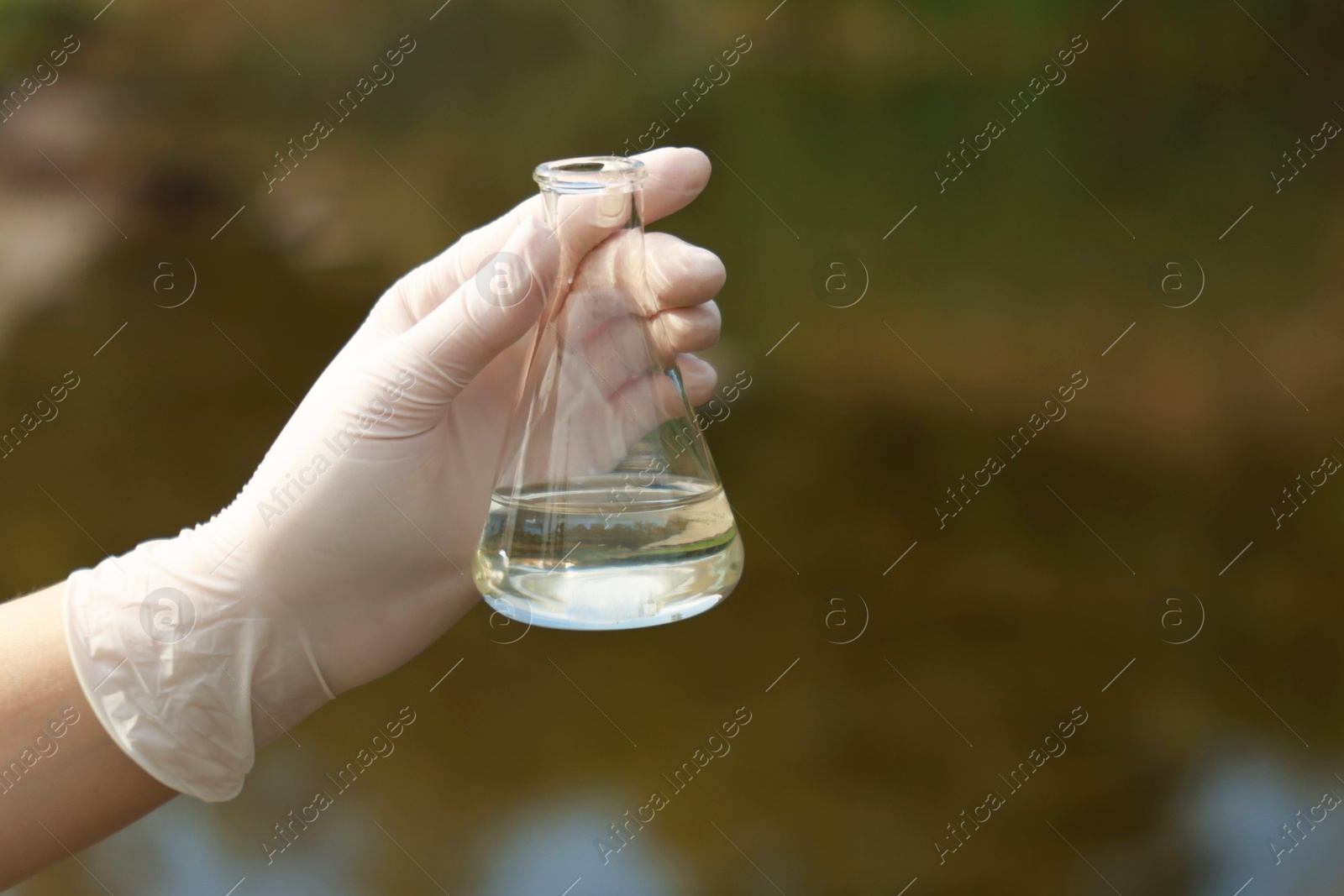 Photo of Examination of water quality. Researcher holding flask with sample outdoors, closeup