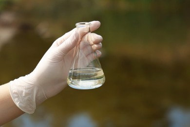 Photo of Examination of water quality. Researcher holding flask with sample outdoors, closeup