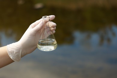 Photo of Examination of water quality. Researcher holding flask with sample outdoors, closeup. Space for text