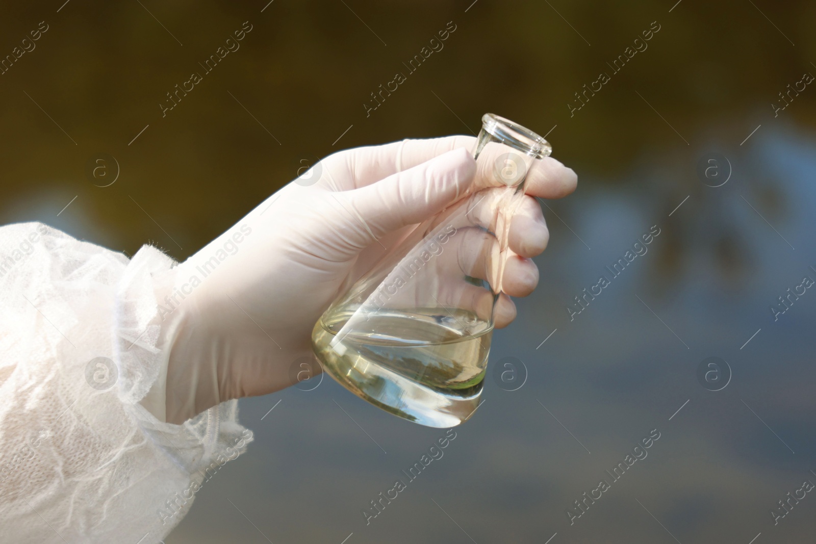 Photo of Examination of water quality. Researcher holding flask with sample outdoors, closeup