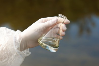 Photo of Examination of water quality. Researcher holding flask with sample outdoors, closeup