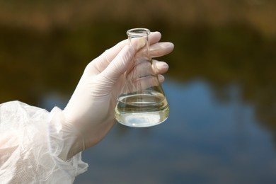 Photo of Examination of water quality. Researcher holding flask with sample outdoors, closeup