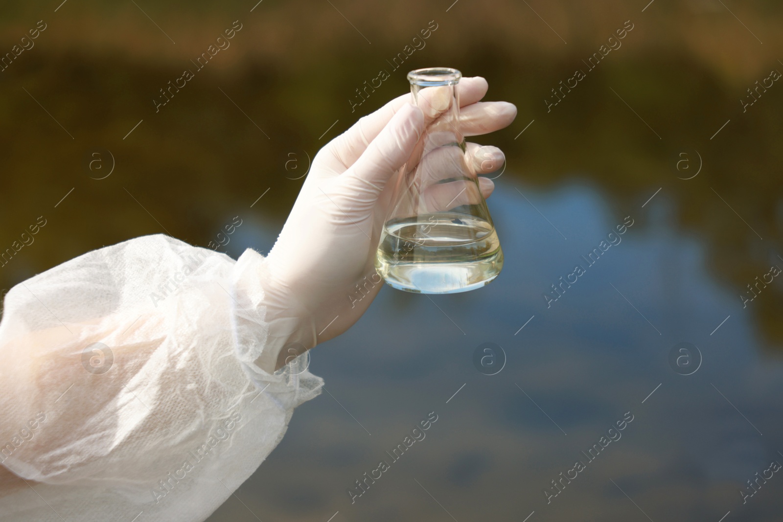 Photo of Examination of water quality. Researcher holding flask with sample outdoors, closeup