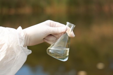 Photo of Examination of water quality. Researcher holding flask with sample outdoors, closeup