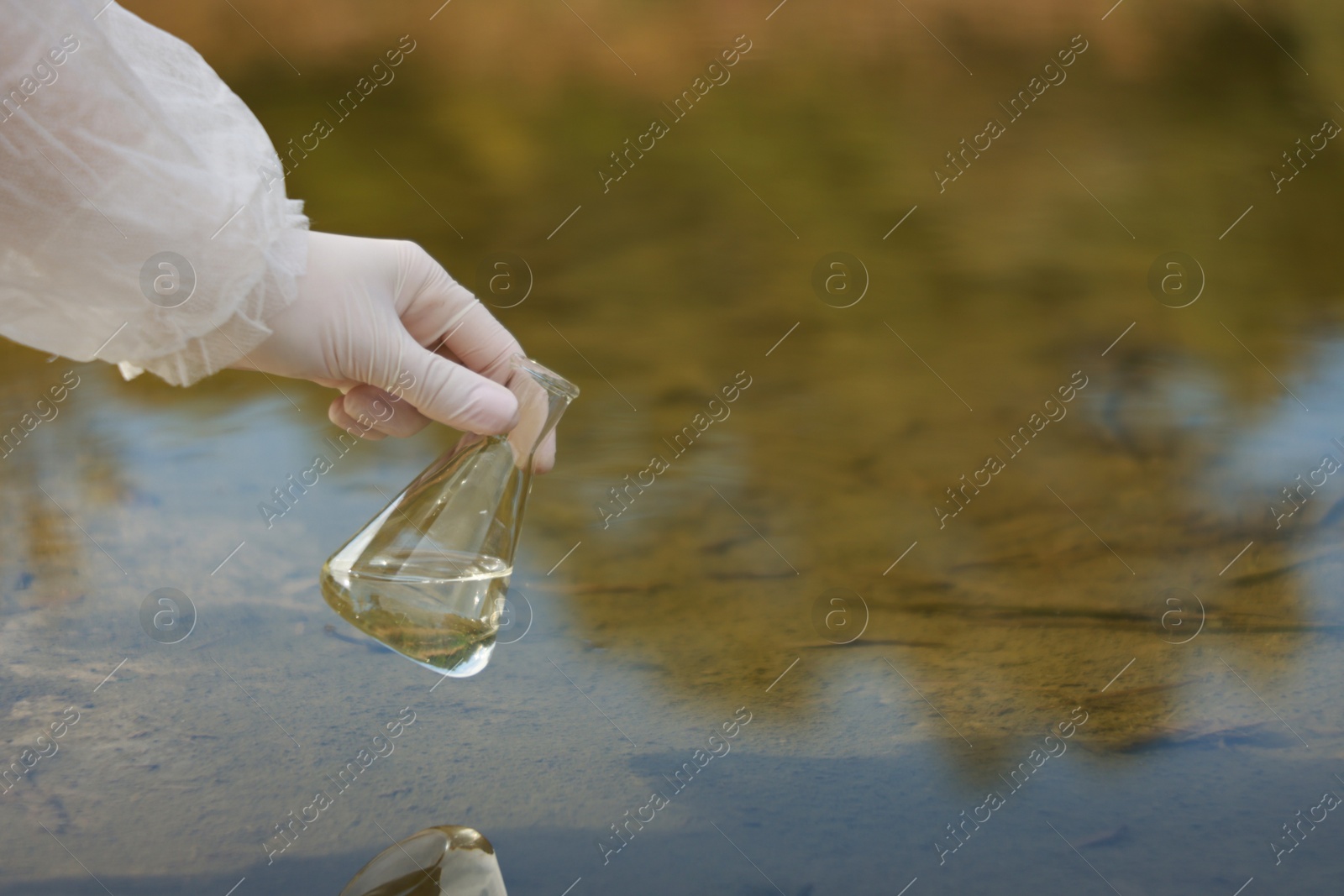 Photo of Examination of water quality. Researcher holding flask with sample from lake outdoors, closeup. Space for text