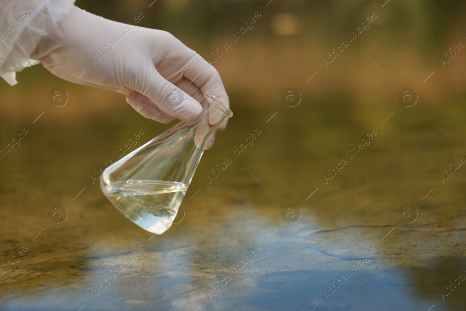 Photo of Examination of water quality. Researcher holding flask with sample from lake outdoors, closeup. Space for text