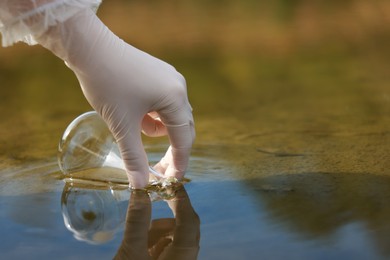 Photo of Examination of water quality. Researcher taking water sample from lake outdoors, closeup. Space for text