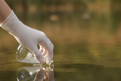 Photo of Examination of water quality. Researcher taking water sample from lake outdoors, closeup. Space for text