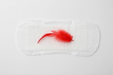 Photo of Menstrual pad with red feather on white background, top view