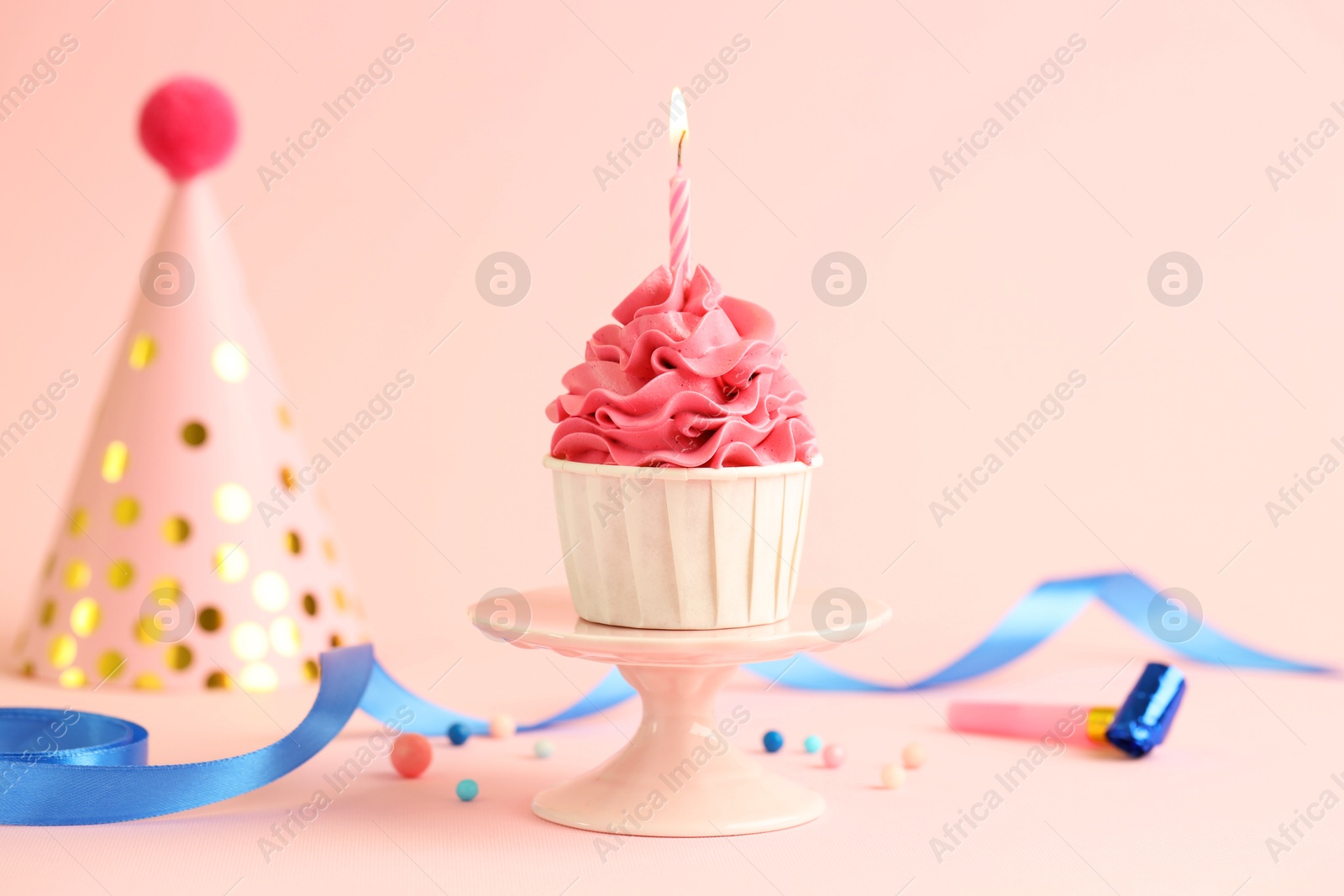 Photo of Tasty cupcake with burning candle and party cone on pink background