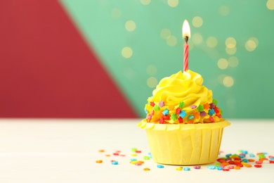 Photo of Tasty cupcake with burning candle on color background with blurred lights, space for text