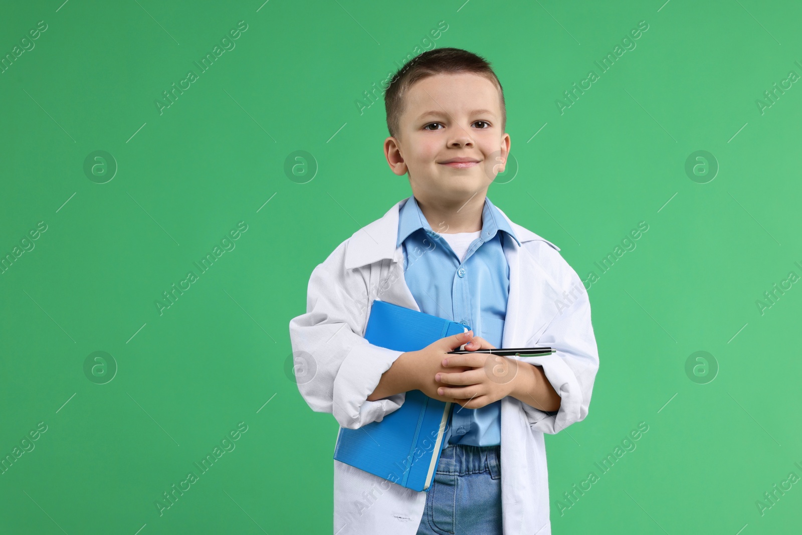 Photo of Little boy with book pretending to be doctor on green background. Dreaming of future profession