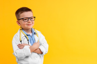 Photo of Little boy with stethoscope pretending to be doctor on yellow background, space for text. Dreaming of future profession