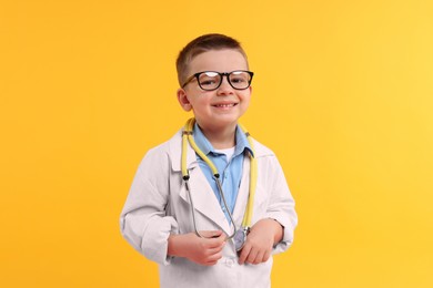 Little boy with stethoscope pretending to be doctor on yellow background. Dreaming of future profession