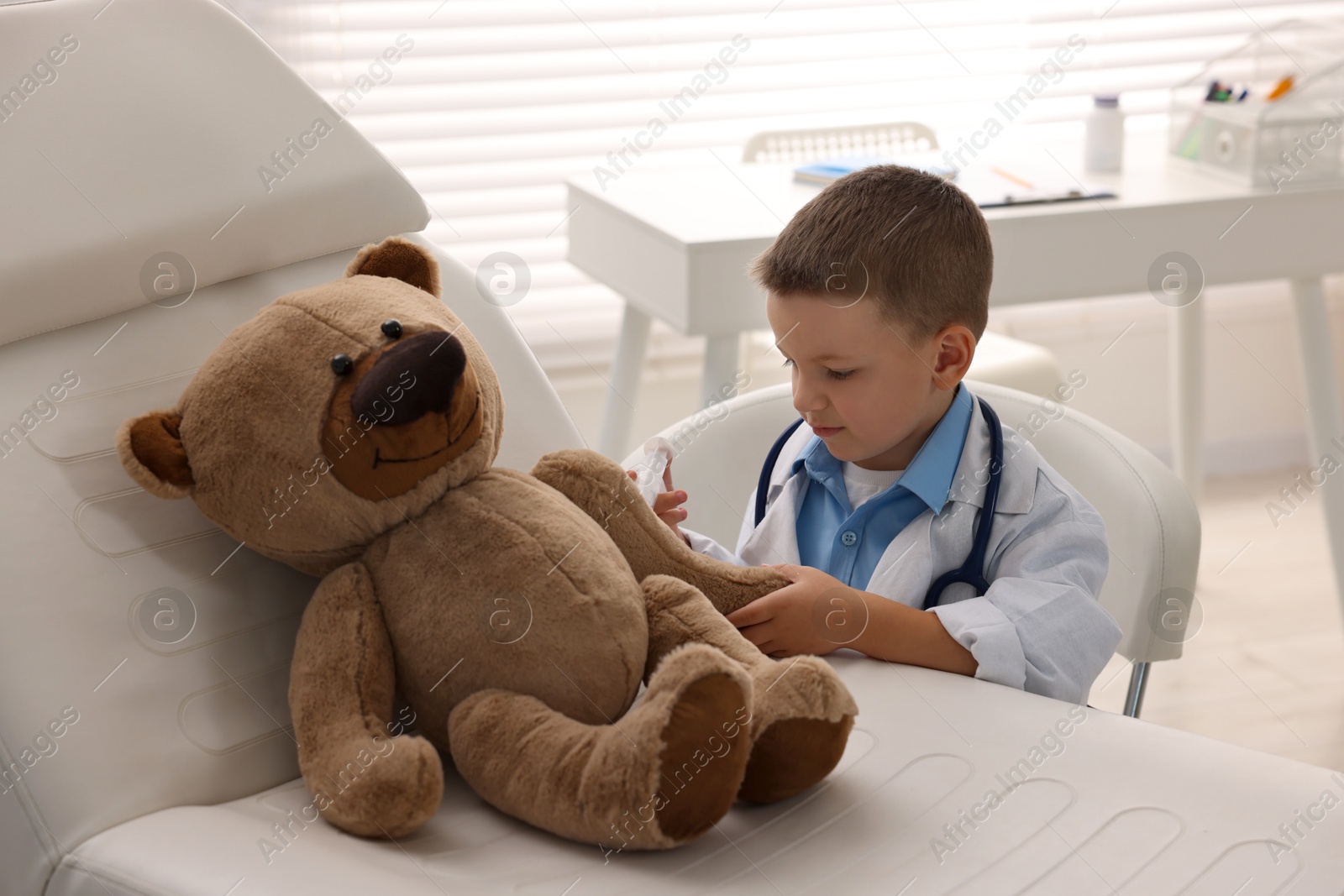 Photo of Little boy with stethoscope, syringe and toy pretending to be doctor indoors