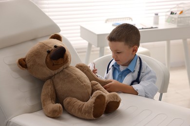 Little boy with stethoscope, syringe and toy pretending to be doctor indoors