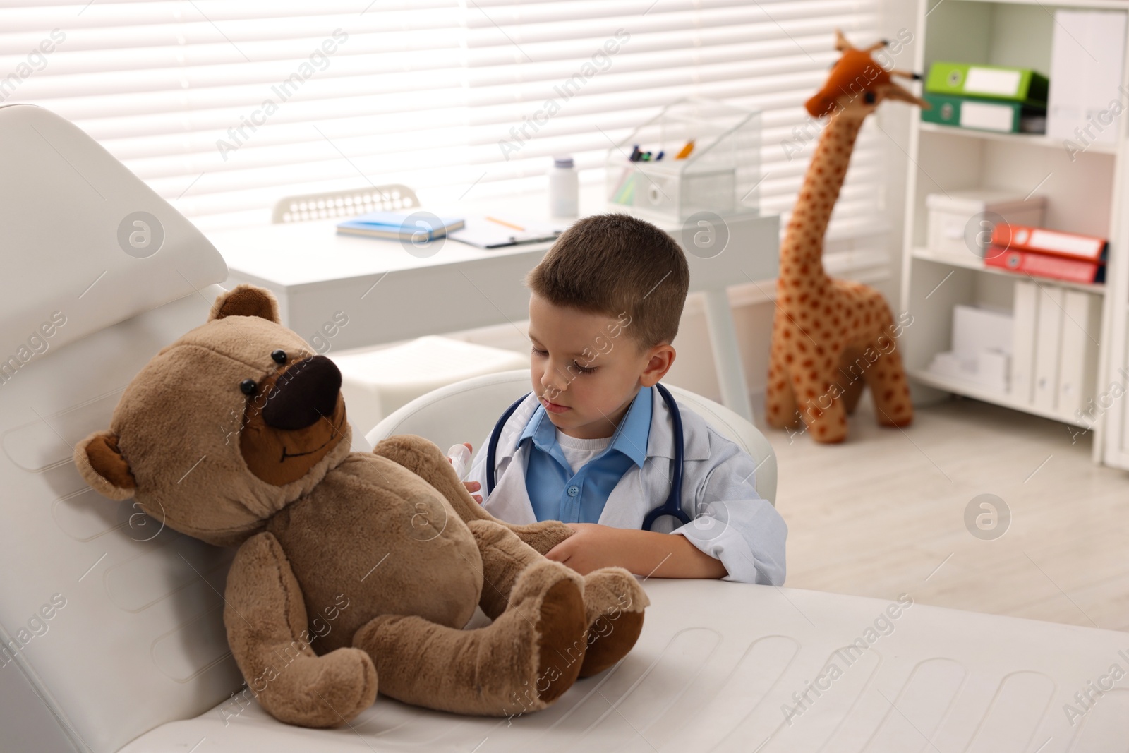 Photo of Little boy with stethoscope, syringe and toy pretending to be doctor indoors